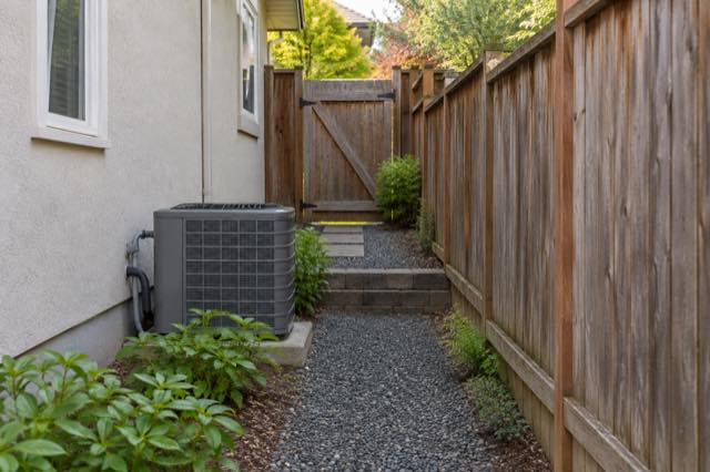 Narrow residential side access between a fence and stucco house.