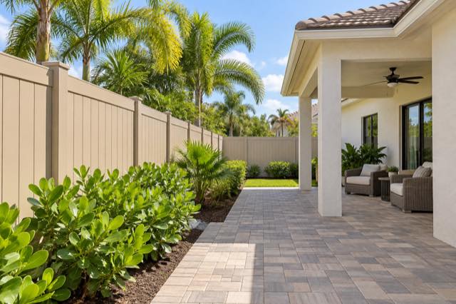 Tan vinyl privacy fencing around a tidy paver seating area beside a stucco home.